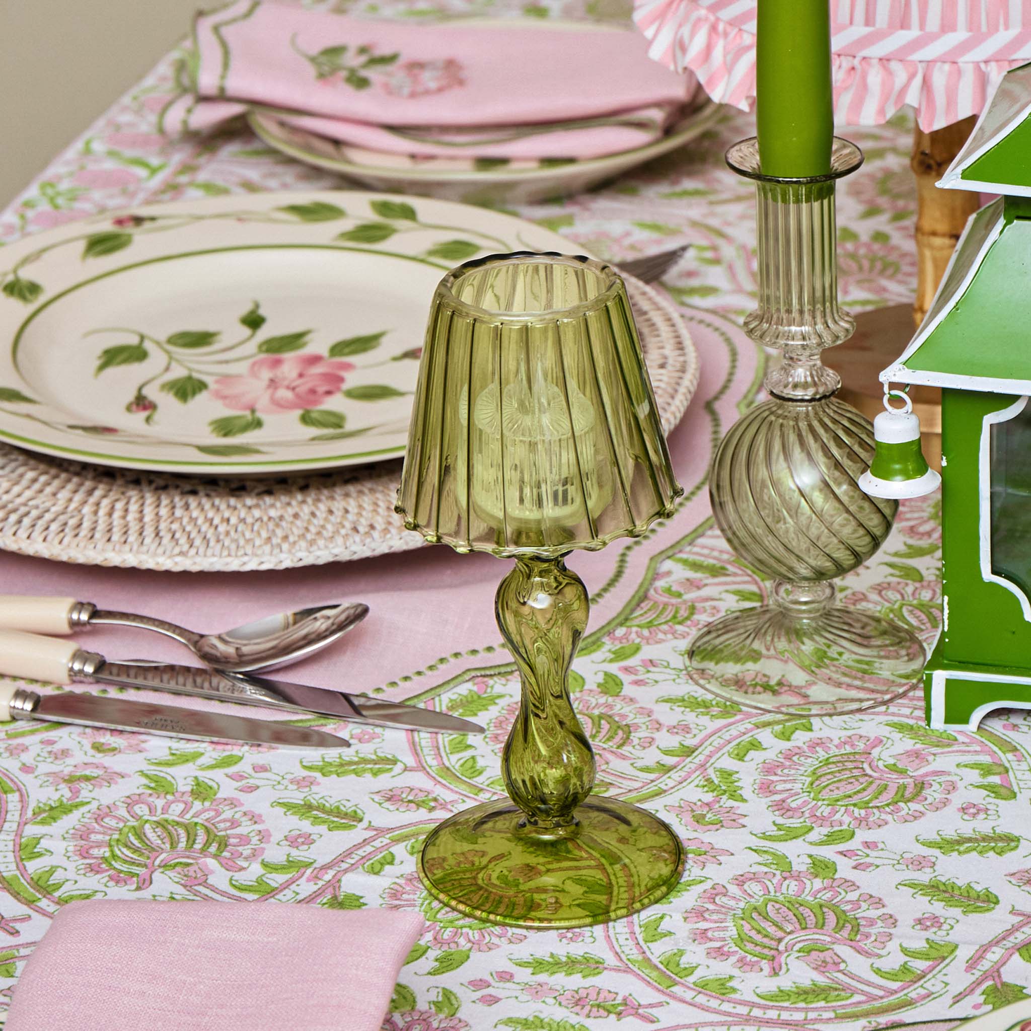 Decorative green table lamp on a patterned tablecloth with floral plates and pink napkins.