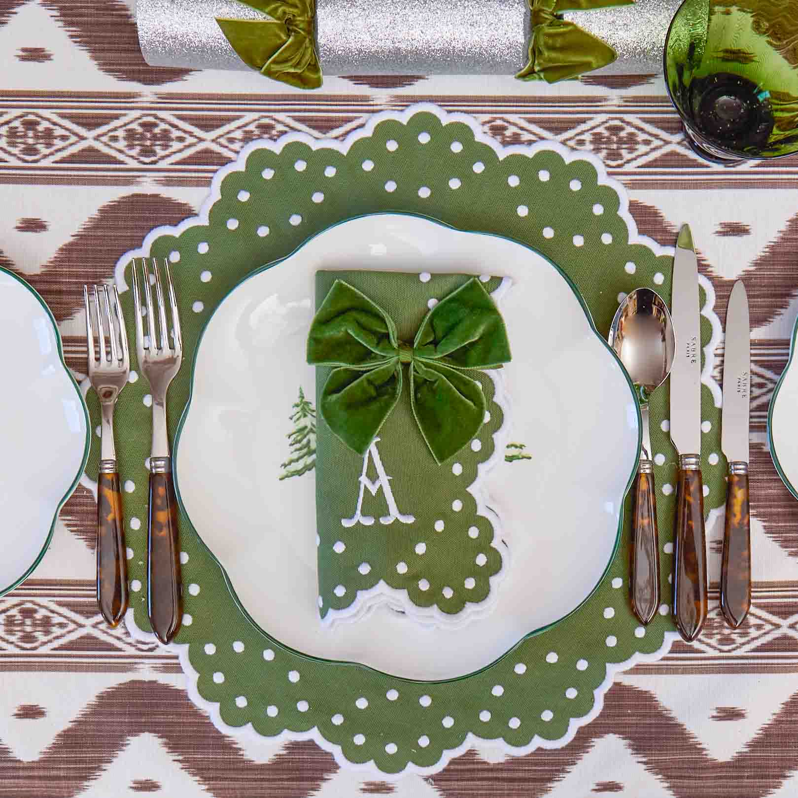 Green and white place setting with a decorative bow on a patterned tablecloth.