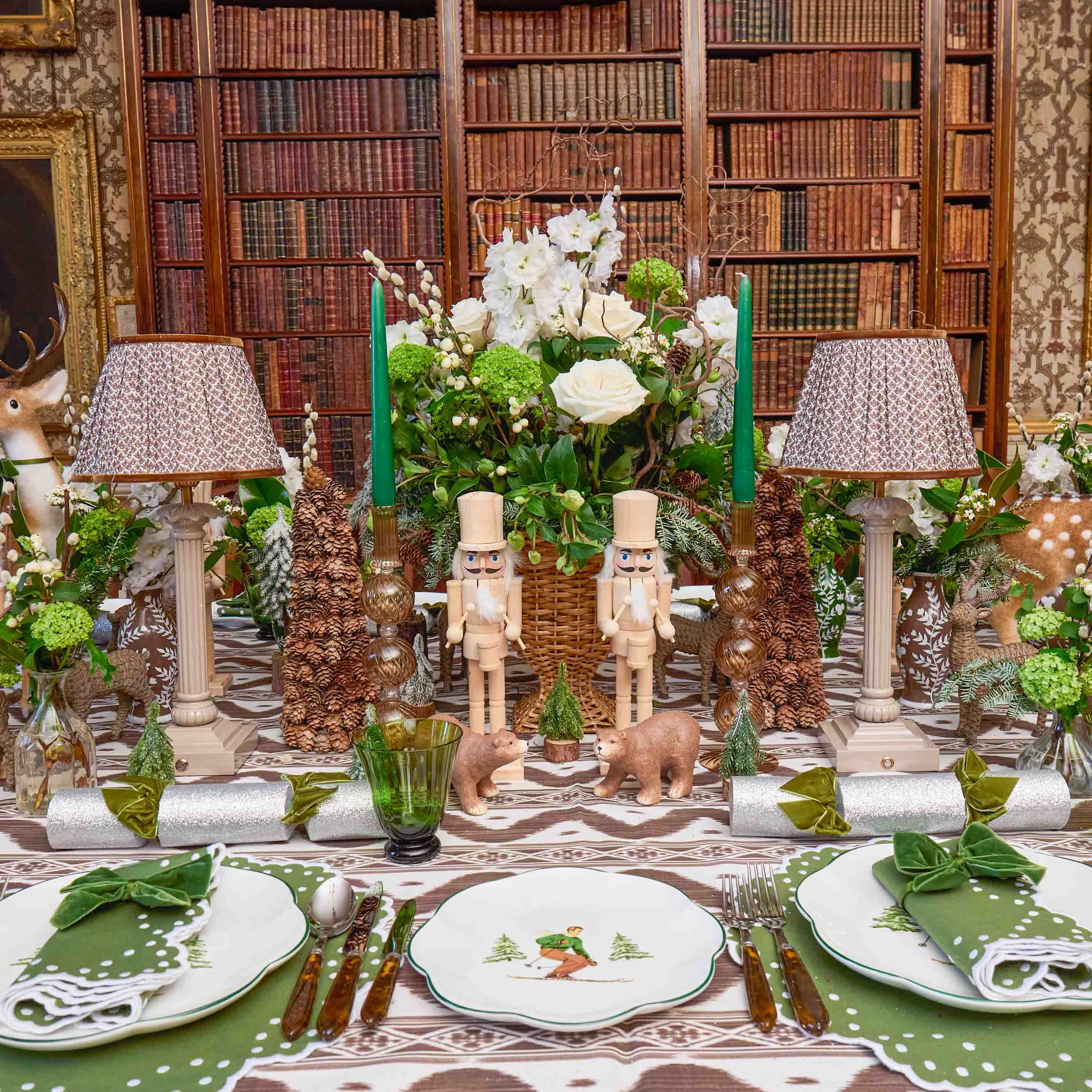 Decorative table setting with nutcrackers, flowers, and candles in a room with bookshelves.