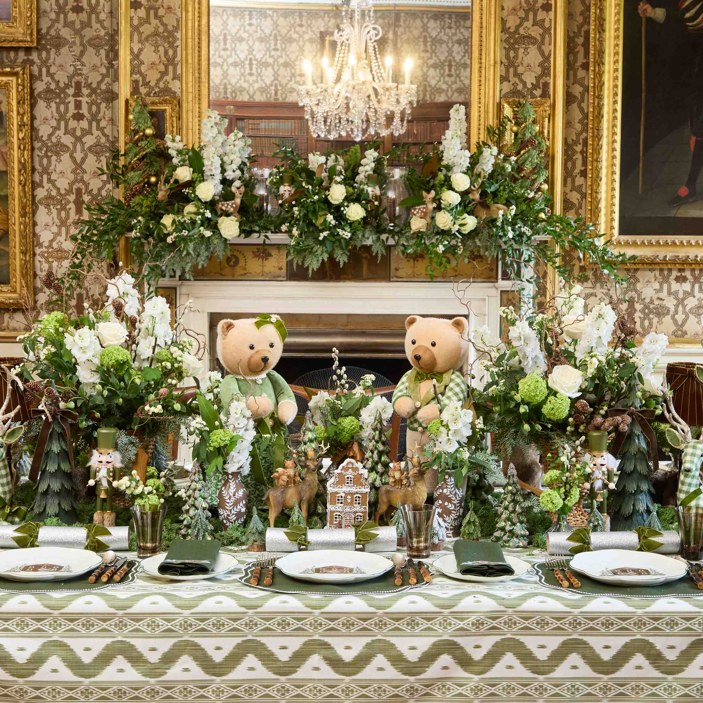 Decorative table setting with teddy bears, flowers, and small houses in an elegant room.