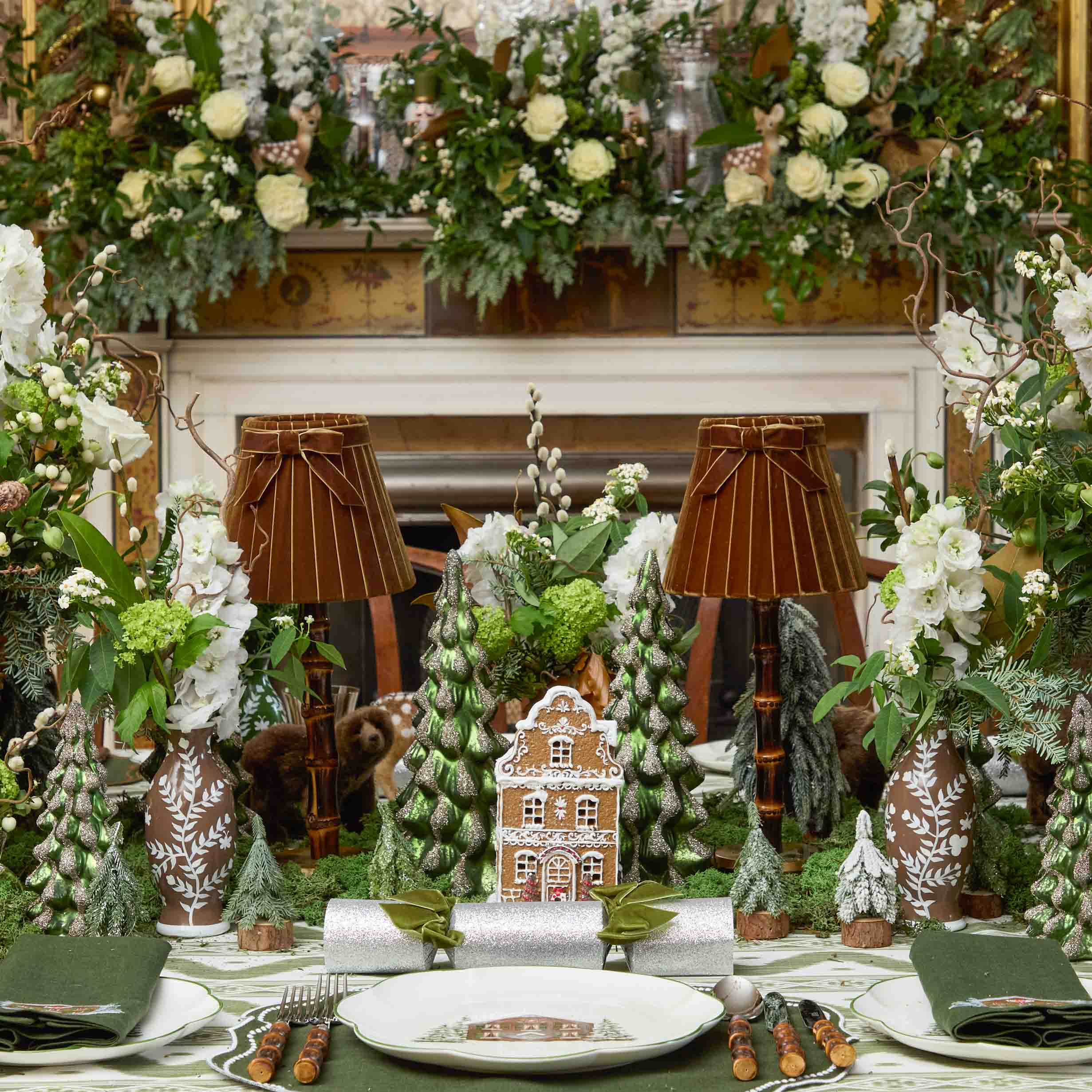 Decorative table setting with gingerbread house, Christmas trees, and floral arrangements.