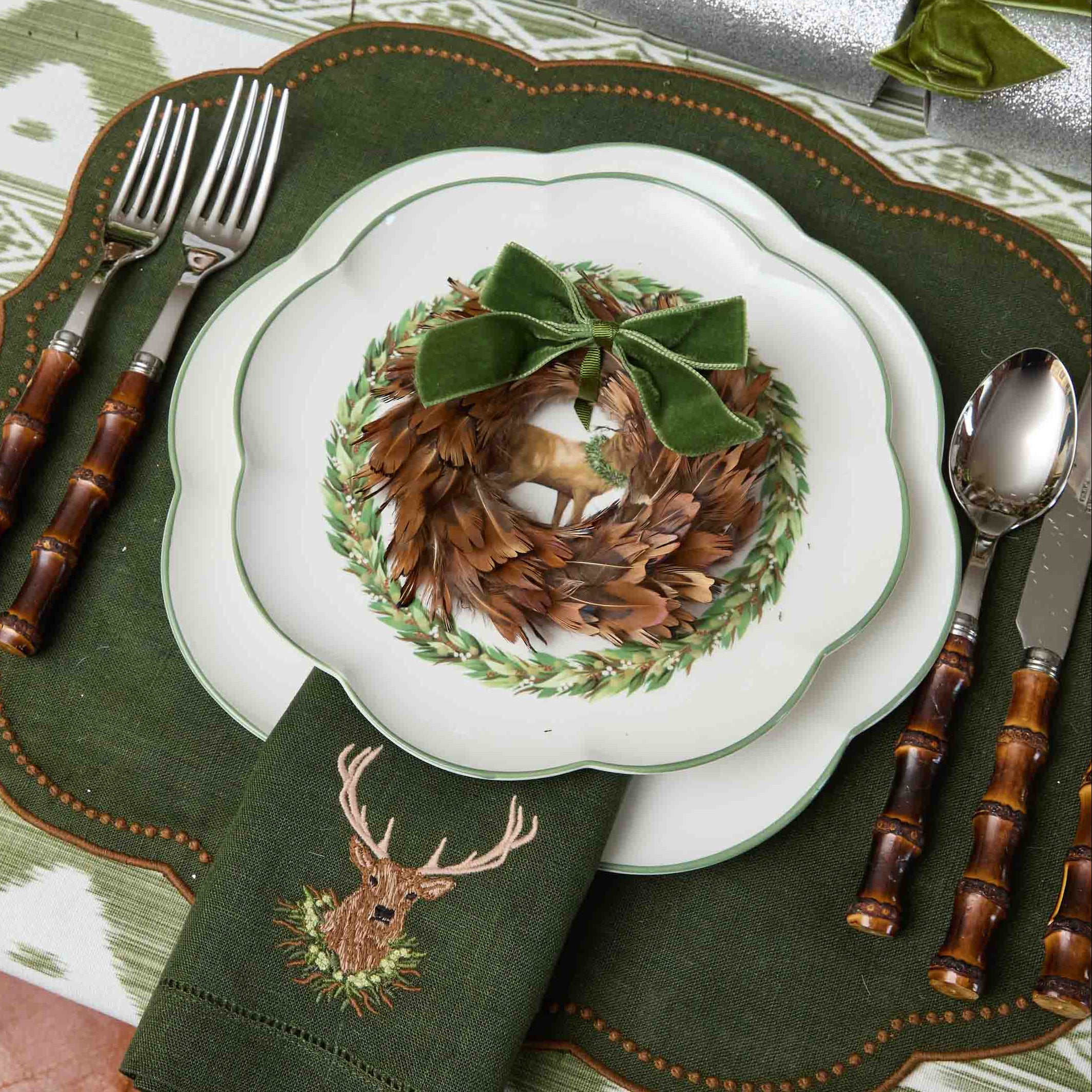 Christmas table setting with green placemat, white plate with wreath, and decorative napkin.