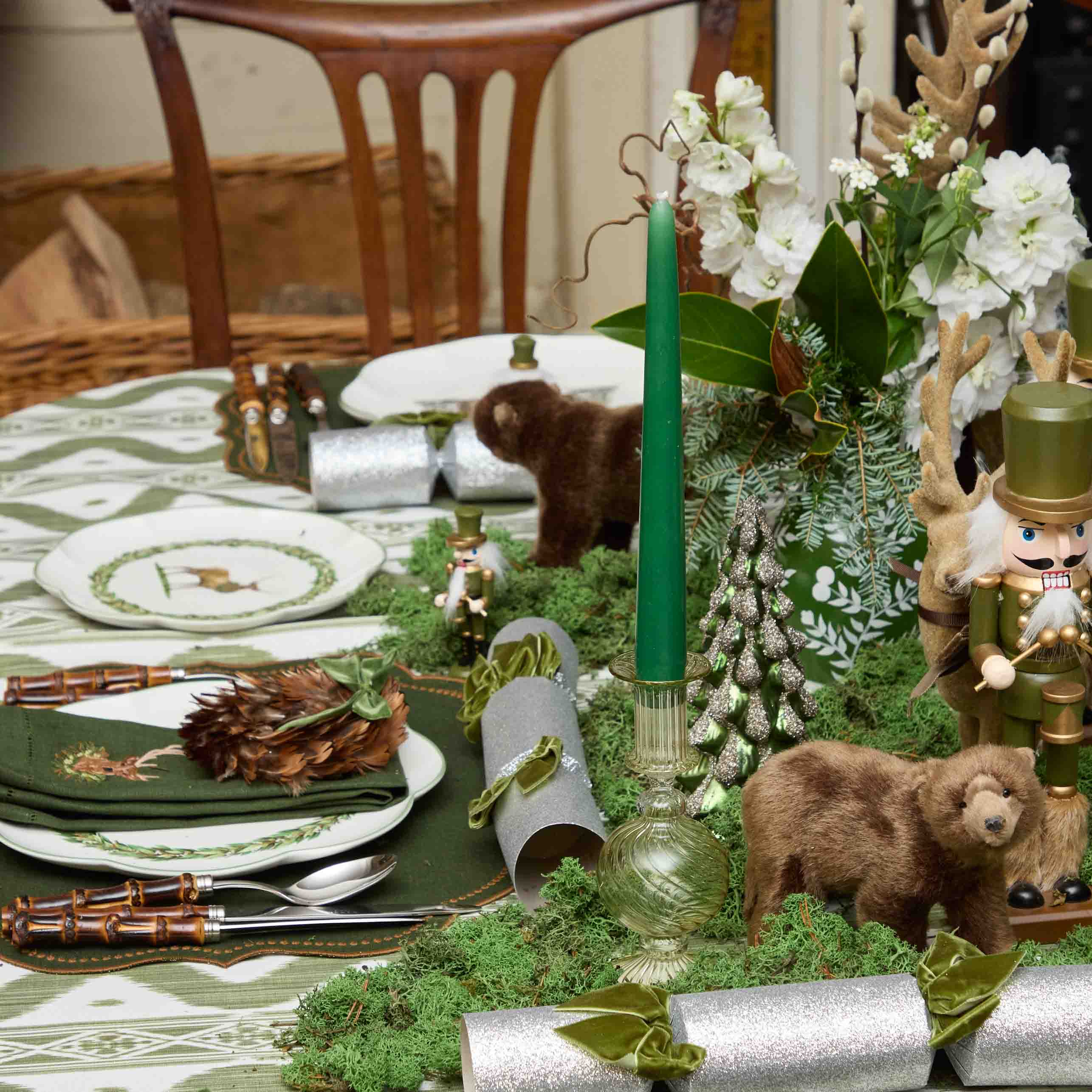 Decorative table setting with green candles, bears, and floral arrangements.