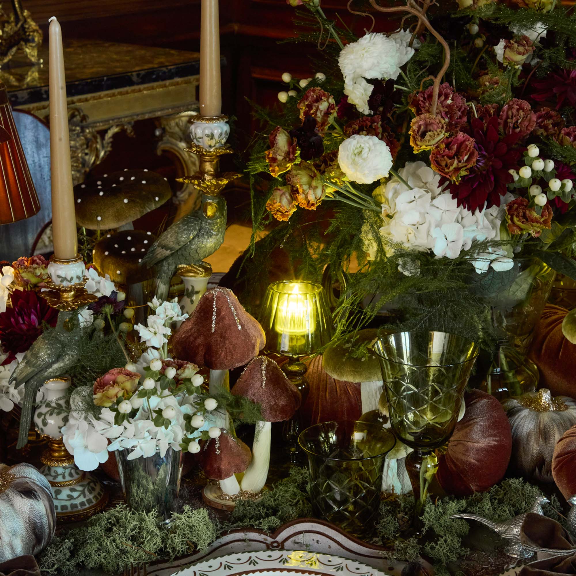 Decorative table setting with candles, flowers, and glassware in a warm, ambient setting.
