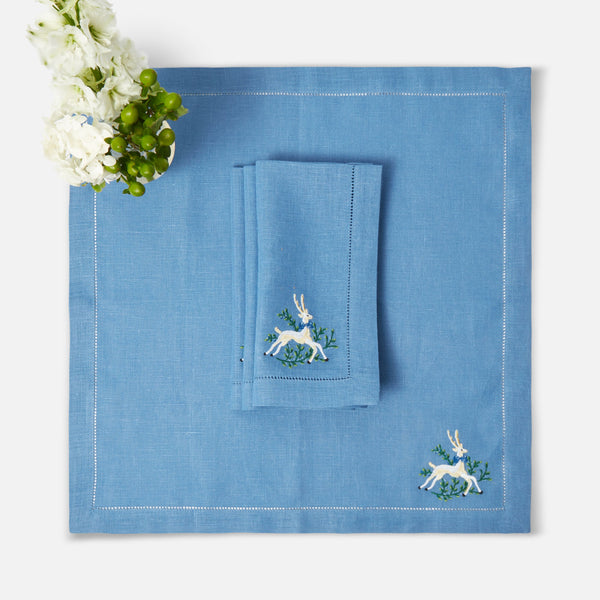 Set of 4 blue linen napkins with delicate embroidered prancing deer motifs.