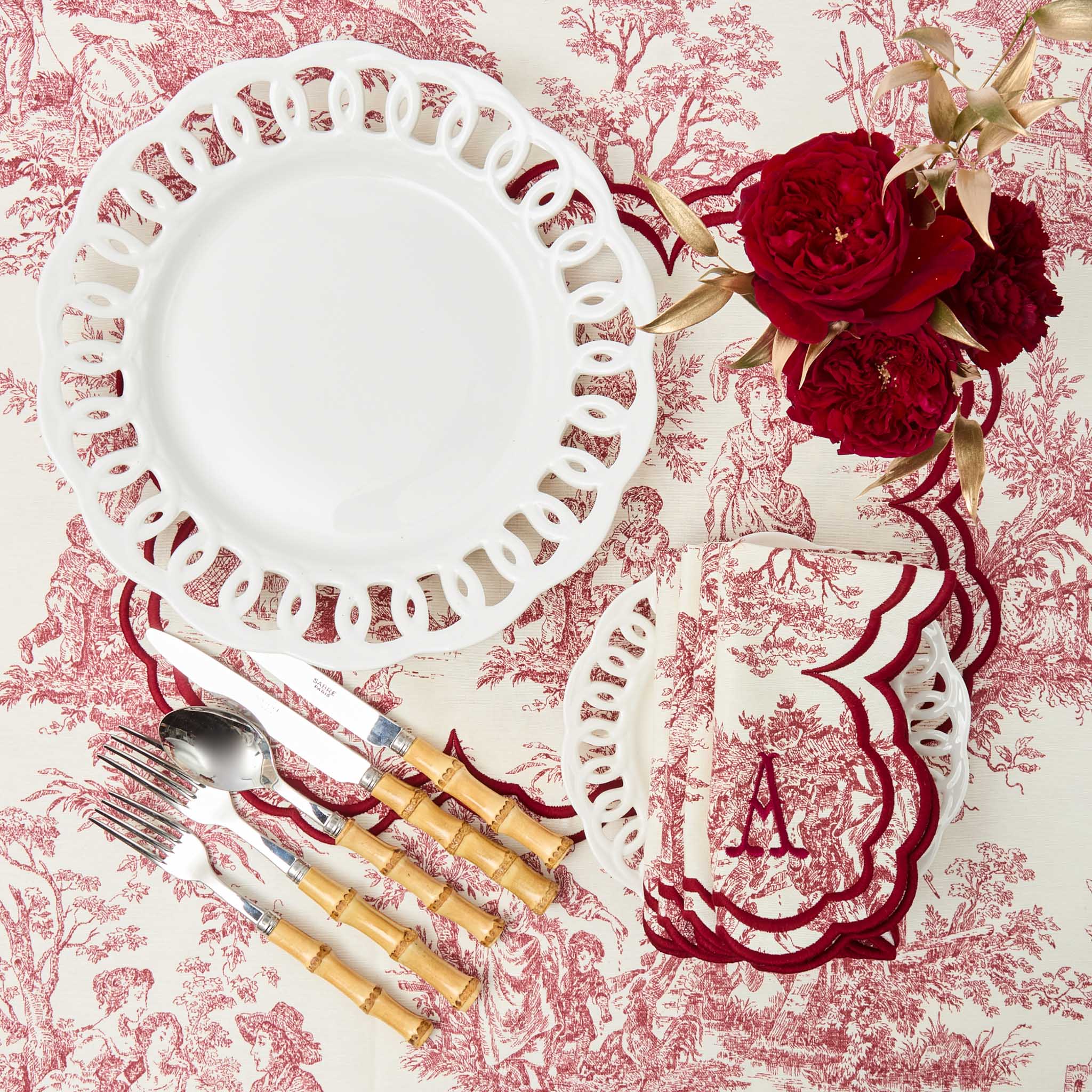 Table setting with white plate, red roses, and cutlery on a floral tablecloth.