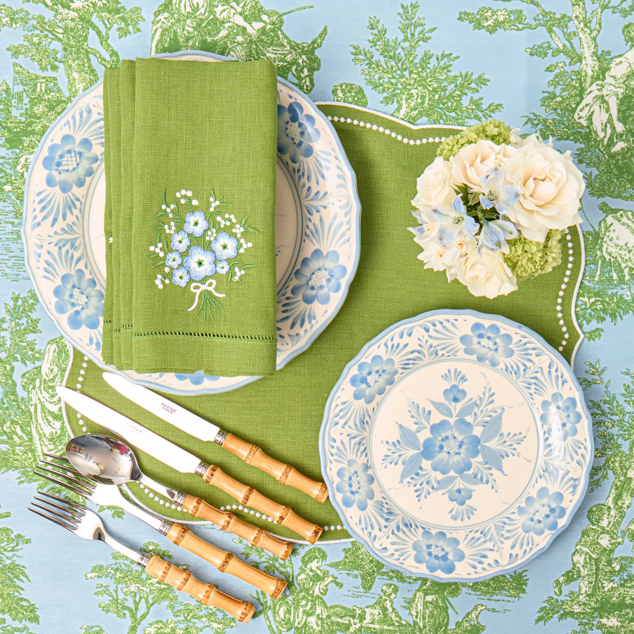 Table setting with floral plates, green napkin, and cutlery on a decorative tablecloth.