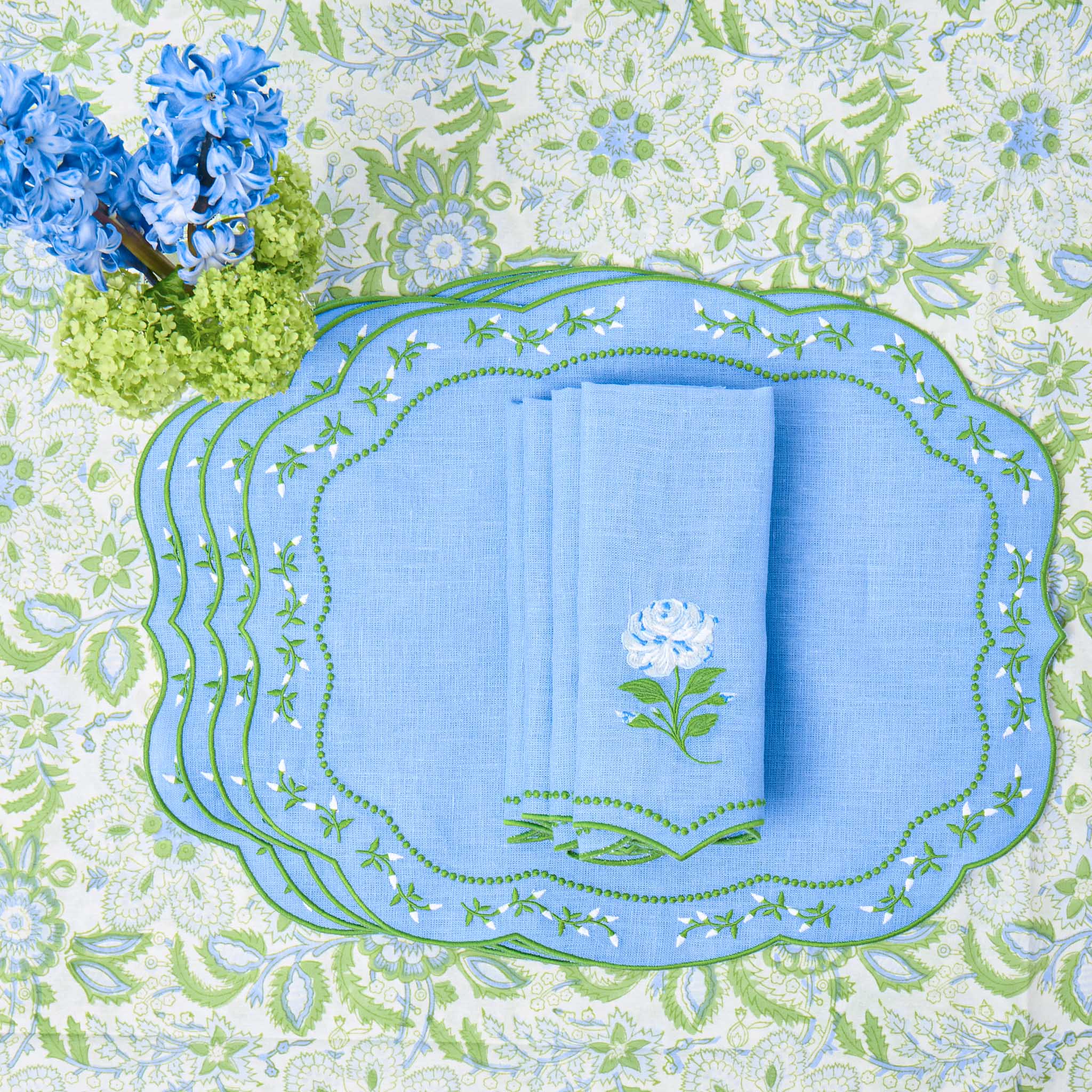 Set of blue napkins with floral embroidery on a decorative tablecloth with floral patterns.