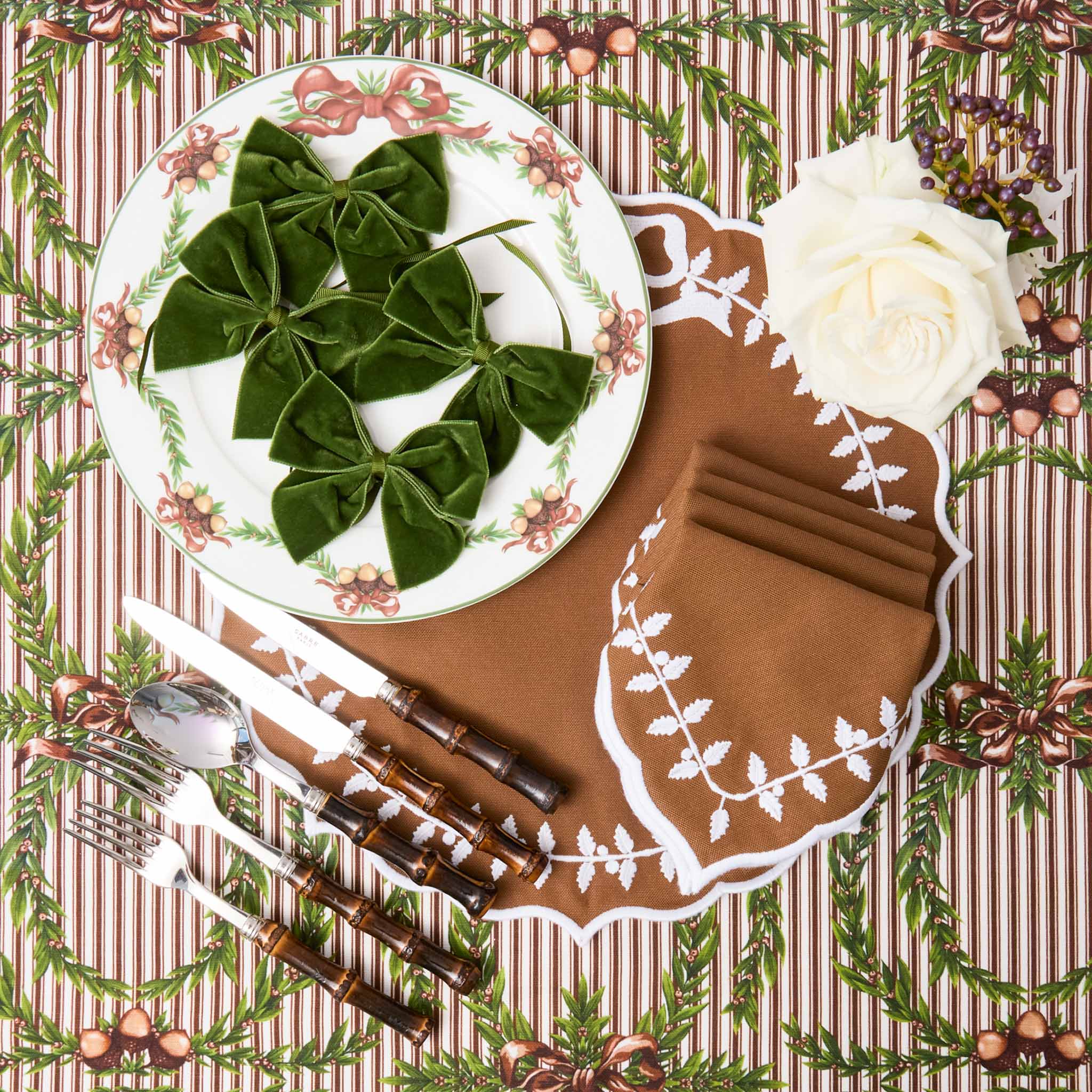 Decorative table setting with a plate of green leaves, white flowers, and cutlery on a patterned tablecloth.