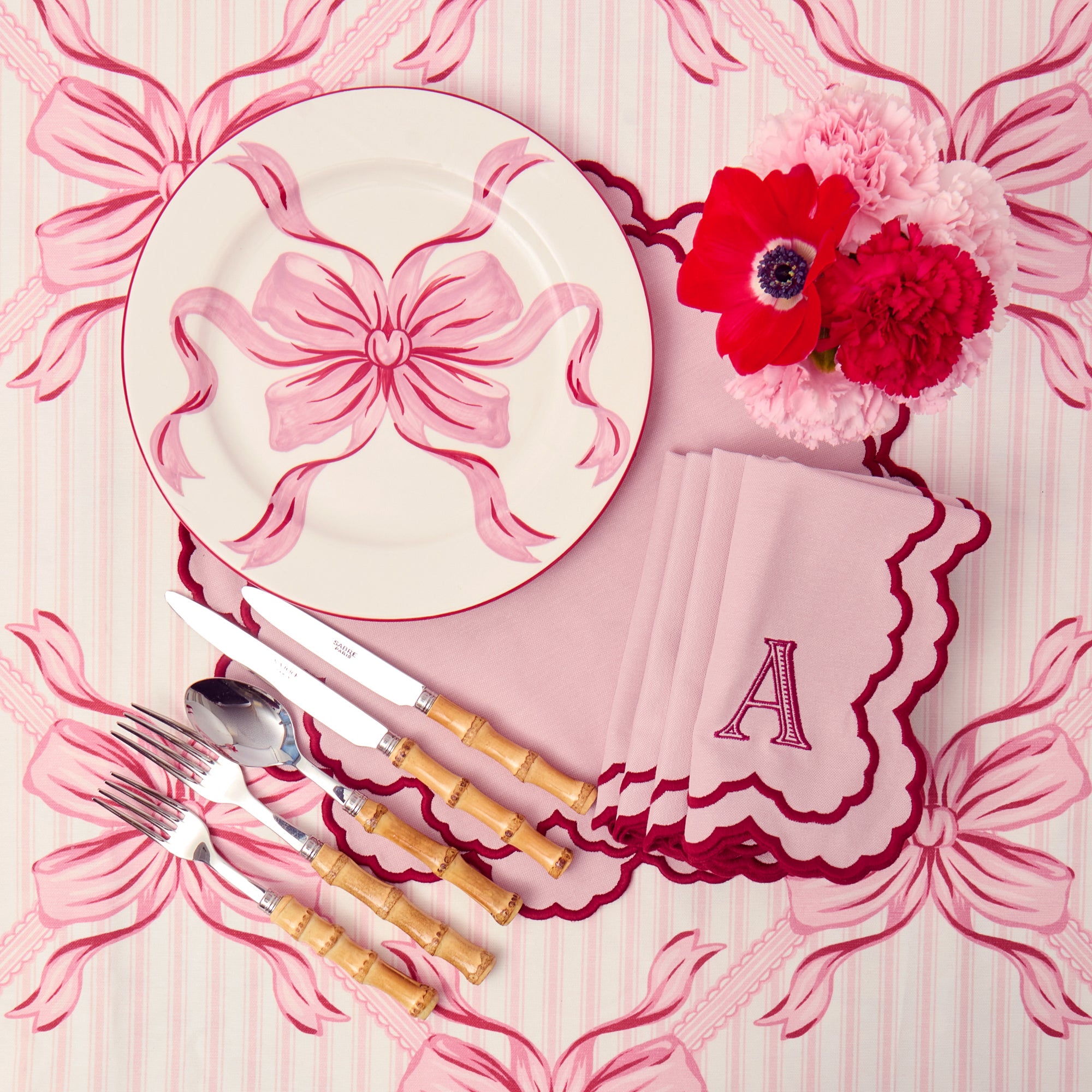 Pink and white table setting with a decorative plate, cutlery, and floral arrangement on a matching pink background.