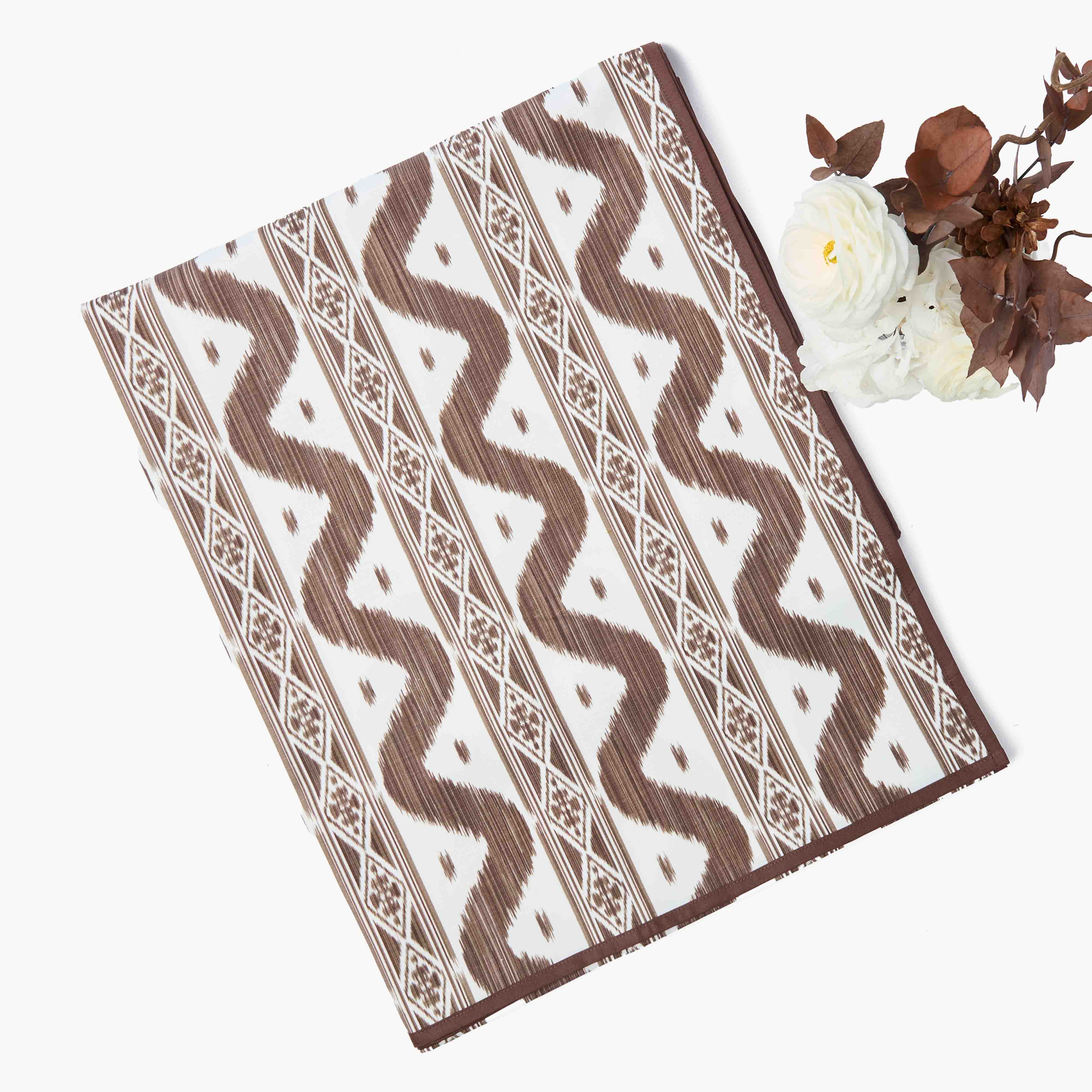 Ikat print brown and white patterned placemats on a white surface with flowers and leaves.