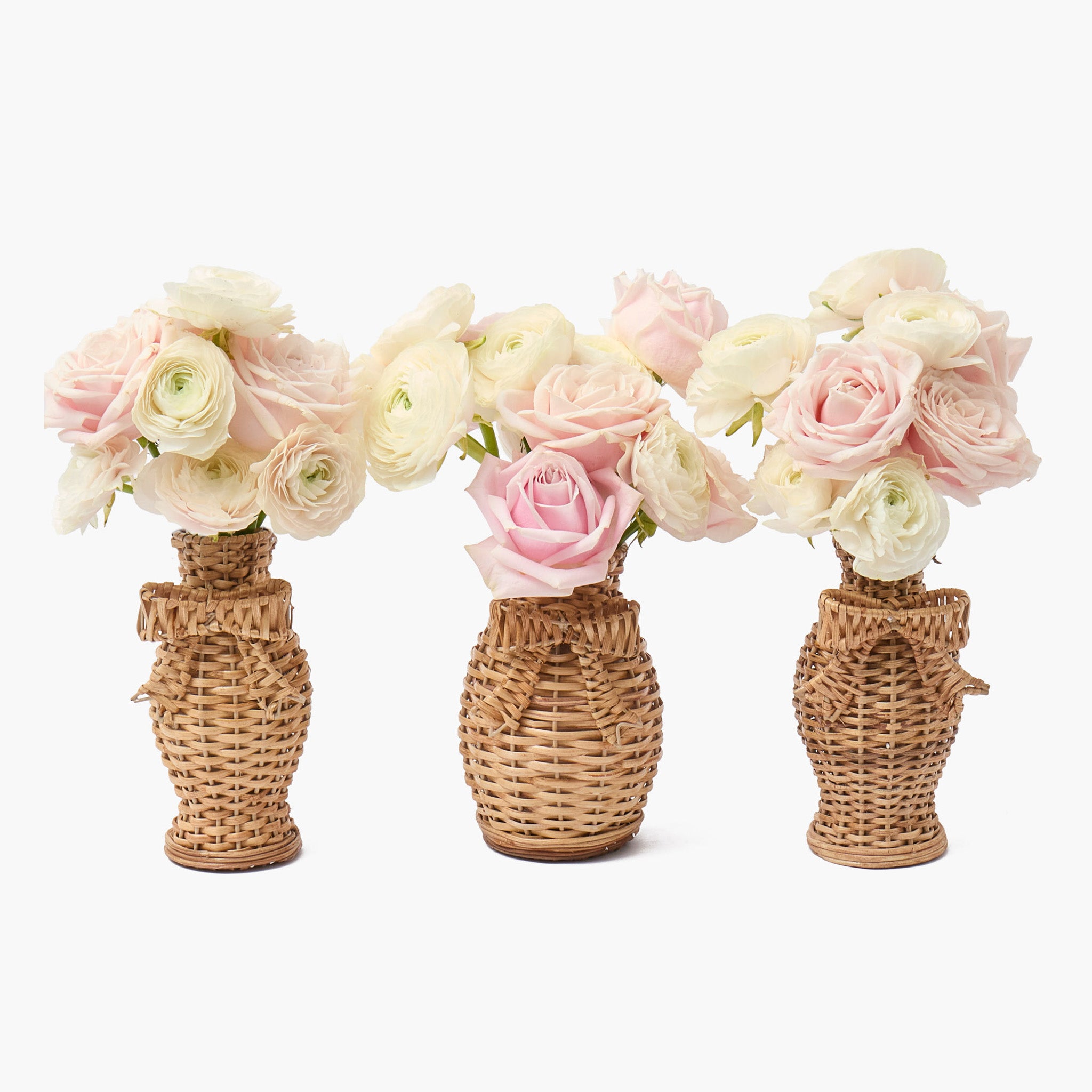 Three rattan wicker vases with pink and white flowers on a white background